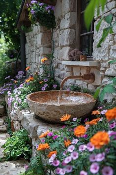 a stone bowl sink sitting on top of a rock wall next to flowers and plants