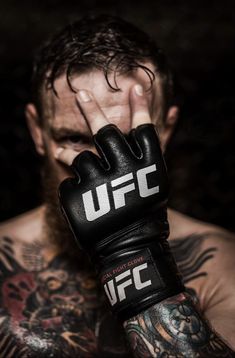 a man with tattoos on his arm wearing boxing gloves and holding his hand up to his face