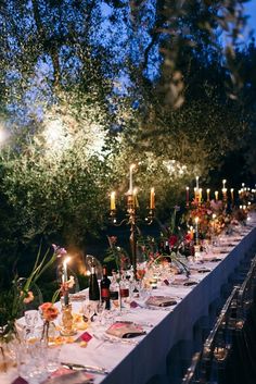 a long table is set up with candles and wine glasses for an outdoor dinner party