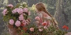 a woman with braids standing in front of pink and red flowered planters