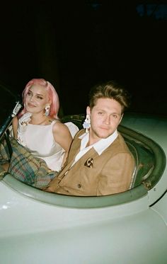 a man and woman sitting in the back of a car at night with pink hair