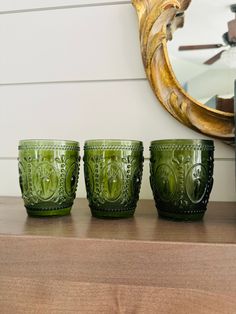 three green glass cups sitting on top of a wooden table