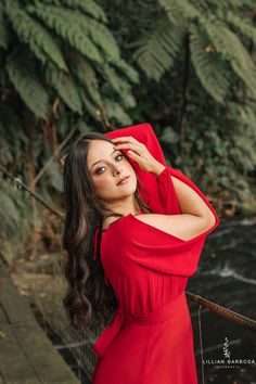 a woman in a red dress is posing for a photo on a bridge over a river