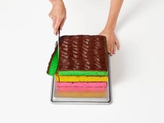 a person is cutting into a cake with colored frosting on it and holding a knife