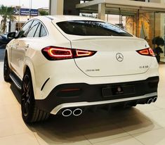 the rear end of a white mercedes car in a showroom with people looking at it