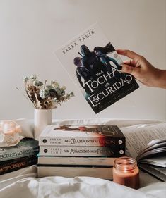 a person is holding up a book in front of some books on a bed with white sheets