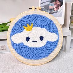 a blue and white cross - stitch hoop with a yellow crown on it, sitting next to a framed photo