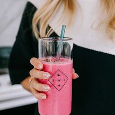 a woman holding a pink smoothie in her right hand and a straw in her other hand