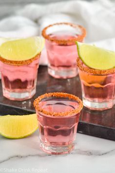 three glasses filled with pink and yellow cocktails on top of a tray next to lime slices