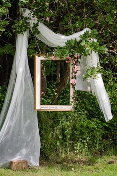 a mirror hanging from the side of a tree next to a lush green forest filled with flowers