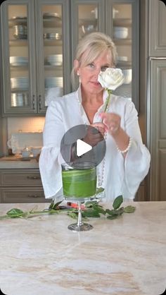 a woman is holding a rose in her hand while standing at a kitchen counter top