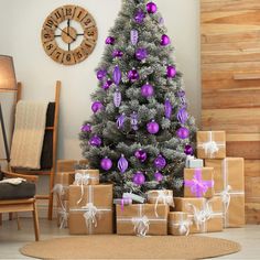 a decorated christmas tree with purple ornaments and presents in front of a clock on the wall