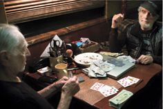 two older men sitting at a table with cards and pens in front of them,