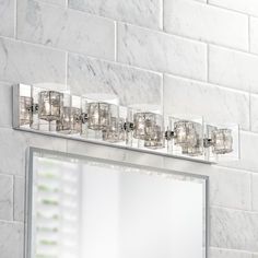 a bathroom vanity with a mirror and lights on the wall next to it in front of a white tiled wall