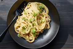 a black plate topped with pasta and peas next to a fork on top of a wooden table