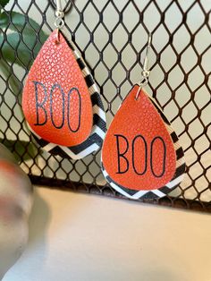 two orange and black earrings with the words boo on them hanging from a wire net