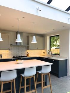 a kitchen with white counter tops and stools next to an open floor plan area