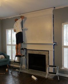 a man standing on a ladder in front of a fire place and painting the wall