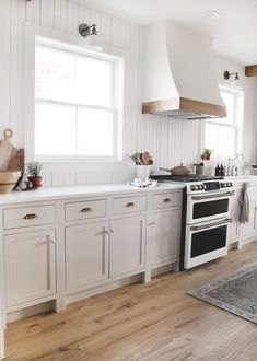 a kitchen with white cabinets and wood flooring is pictured in this image, there are two windows above the stove