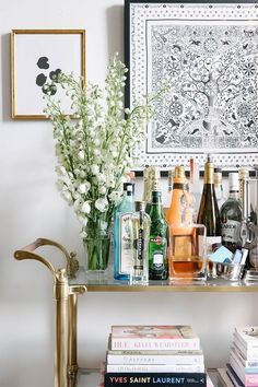 a shelf with books, bottles and vases on it in front of a painting