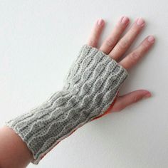 a woman's hand wearing a gray knitted mitt on top of a white wall