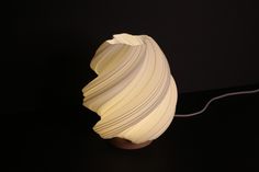 a lamp made out of folded paper on a black surface with a white cord attached to it