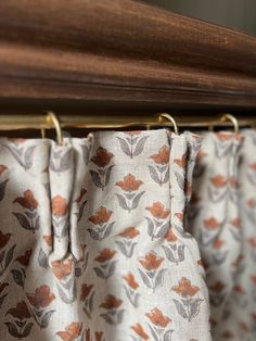 the curtain is hanging on a rod with metal hooks in front of it and an orange flower pattern