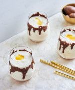 three desserts with chocolate sauce and eggs in them sitting on a marble tray next to gold spoons