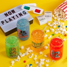 various drinks and snacks on a yellow table with movie tickets, popcorn, and candy