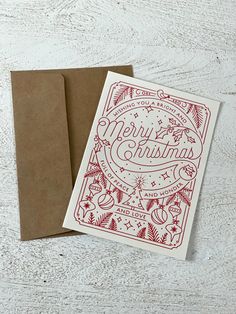 two christmas cards sitting on top of each other next to a brown envelope with red ink