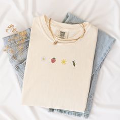 Welcome the sunny days with our Sunkissed Strawberry and Bee Embroidered T-Shirt! Made from 100% cotton Soft Comfort Colors, this shirt is both stylish and comfortable, perfect for your summer adventures.Features:Material: 100% cotton Soft Comfort ColorsSizes: S, M, L, XL, 2XL (refer to size chart in images)Colors Available: Banana, Bay, Blossom, Chalky Mint, Chambray, Ivory, Orchid, Peachy, Violet (Note: Colors may vary slightly due to monitor settings)Design: Summer-inspired embroidery featuring a daisy, strawberry, sun, and bee on the center chestCare Instructions: Machine wash cold, tumble dry lowThis Sunlissed Strawberry and Bee Embroidered T-Shirt is a delightful addition to your wardrobe, bringing a touch of sunshine wherever you go. Perfect for picnics, beach days, or casual outing Trendy Cream Summer T-shirt, Cream Cotton Top With Floral Embroidery, Trendy Summer T-shirt With Embroidered Text, Trendy Embroidered Summer T-shirt, Trendy T-shirt With Embroidered Text For Summer, White Embroidered T-shirt For Summer, Cream Embroidered Cotton Tops, Summer Organic Cotton Cream Tops, Cream Organic Cotton Summer Tops