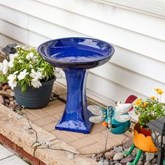 a blue bird bath sitting on the side of a house next to potted plants