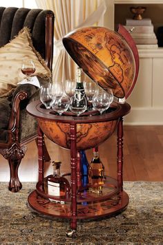 an old world globe with wine glasses and bottles in it on a table next to a couch