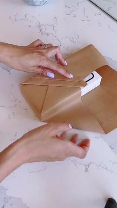 two hands are holding a piece of brown paper on top of a bag that is open