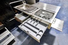 a stainless steel table with an open drawer on the bottom and two trays underneath it