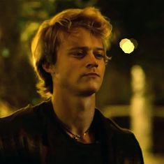 a young man is staring at something in the distance while wearing a black shirt and leather jacket