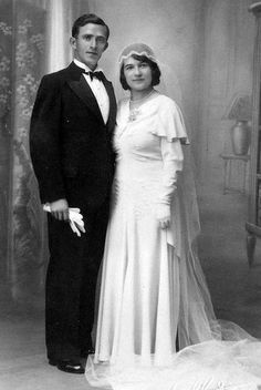 an old black and white photo of a man and woman dressed in formal wear standing next to each other