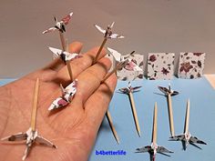 a hand is holding several origami birds on toothpicks and matchesticks