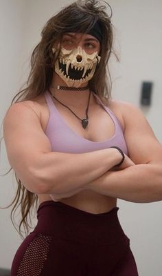 a woman with her arms crossed, wearing a skeleton mask and purple sports bra top