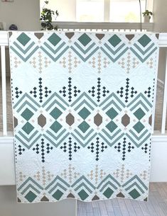 a white and green quilt hanging on a rail in front of a window with potted plants