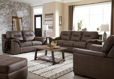 a living room with couches, chairs and a coffee table in front of a brick wall