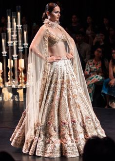 This enchanting earthy beige lehenga set is a beautiful blend of exuberance and grandeur. An ensemble that you will want this wedding season includes a lehenga, a blouse, a dupatta and a veil. Stitched to perfection, the lehenga features 3D embroideries with organza flowers using pearls, salli, cutdana, and stud tassels. The sleeveless blouse features a scintillating sweetheart neckline with handcrafted finish and a back hook closure. Paired with a heavy net dupatta, the cut-work detailing and intricate embroidery take center-stage. The lehenga comes with an attached cancan and the blouse has padding. Completed with a veil, this opulent ensemble silhouette will glimmer in the spotlight. Dry-clean only if required. Slight variation in color is possible due to digital photography. Anarkali-style Hand Embellished Lehenga For Ceremonies, Bollywood Style Beige Raw Silk Lehenga, Traditional Beige Lehenga With Intricate Embroidery, Traditional Drape Lehenga With Intricate Embroidery, Beige Lehenga With Intricate Embroidery, Anarkali Ceremony Sets Hand Embellished, Traditional Drape Beige Embroidered Lehenga, Beige Lehenga With Traditional Drape For Designer Wear, Traditional Hand Embellished Lehenga For Ceremony