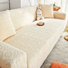 a white couch with pillows and a stuffed animal on it's arm in a living room