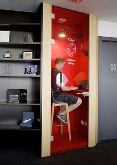 a man sitting at a desk in front of a red wall with shelves on it