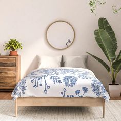 a bed with blue and white comforter next to a potted plant on the floor