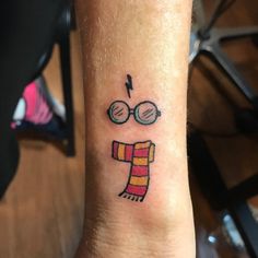 a small tattoo on the wrist of a person with glasses and a scarf around his neck