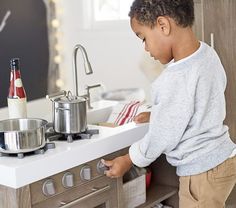 a little boy standing in front of a kitchen counter with pots and pans on it