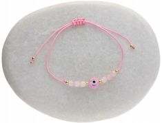 a pink bracelet with an evil eye beaded in gold beads on a white background