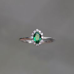 an emerald and diamond ring on a gray background