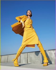 a woman in yellow is posing for the camera with her arms outstretched and legs spread out